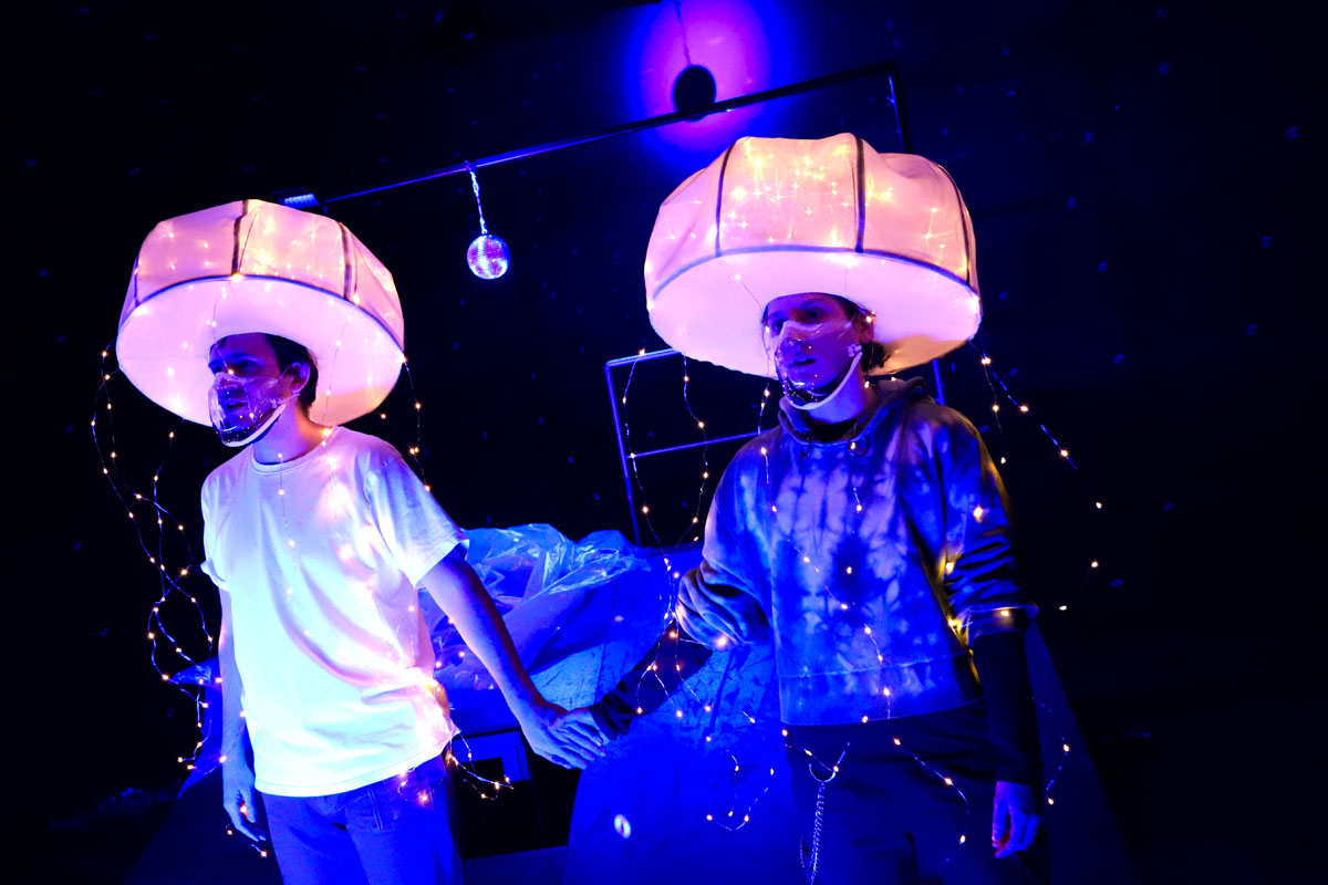Zwei junge Männer mit leuchtenden weißen Hauben auf dem Kopf halten sich an den Händen