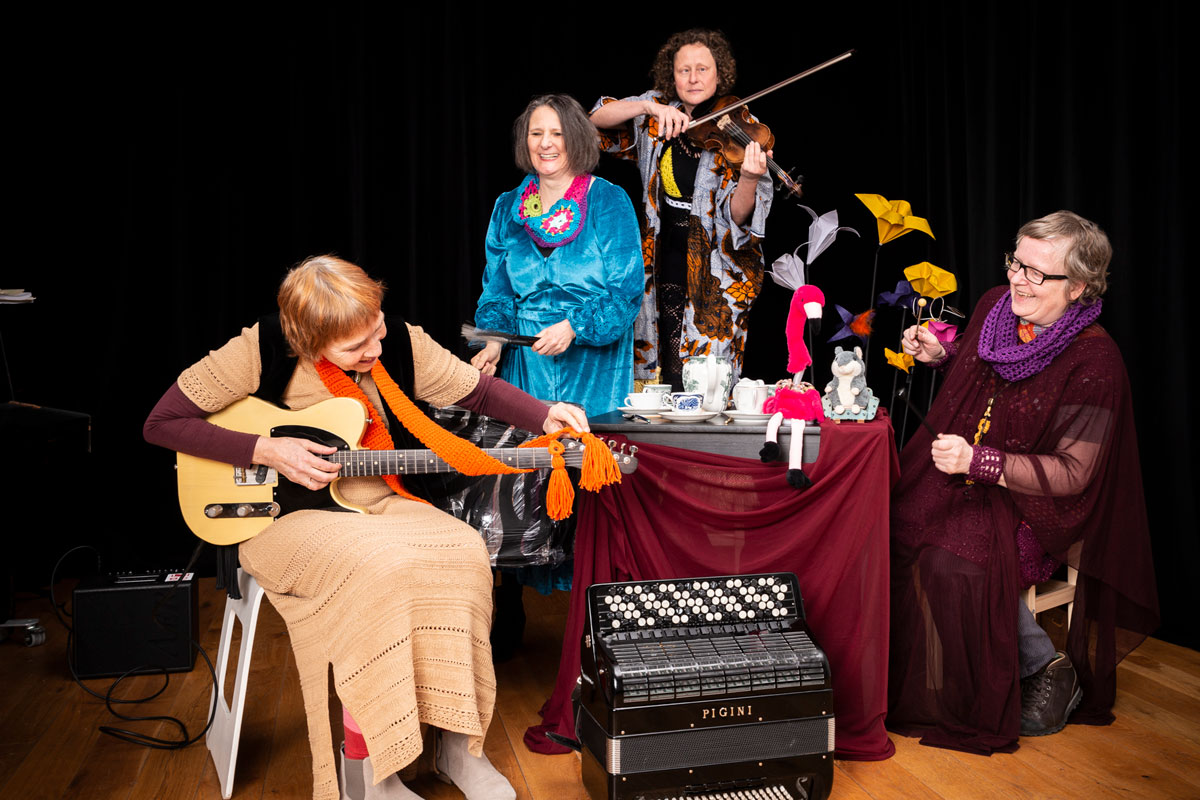 Die vier Musikerinnen des Ensembles Partita Radicale sitzen und stehen an einem gedeckten kleinen Tisch. 