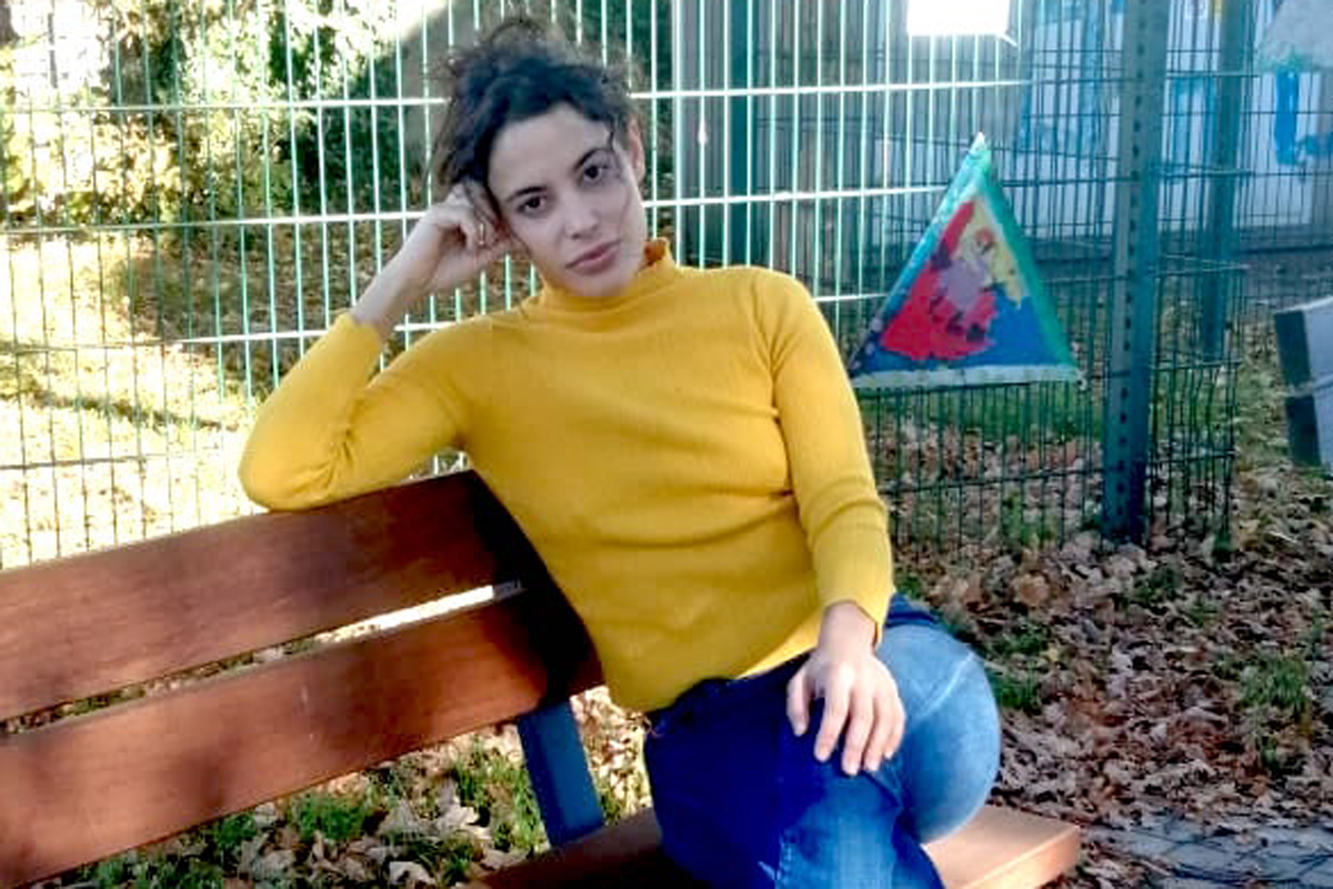 Die Künstlerin Claudia Iglesias sitzt auf einer Bank. Ihr rechter Arm stützt den Kopf