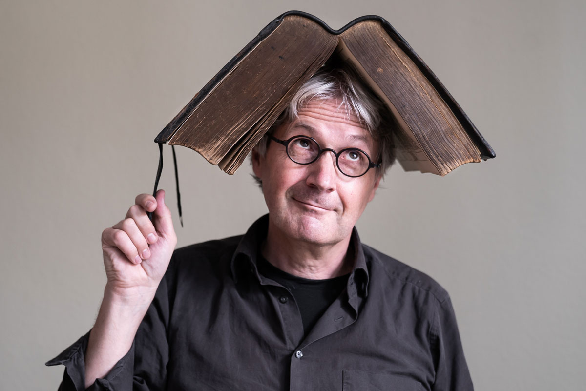 Der Autor Jörg Hilbert trägt ein aufgeklapptes dickes Buch auf seinem Kopf
