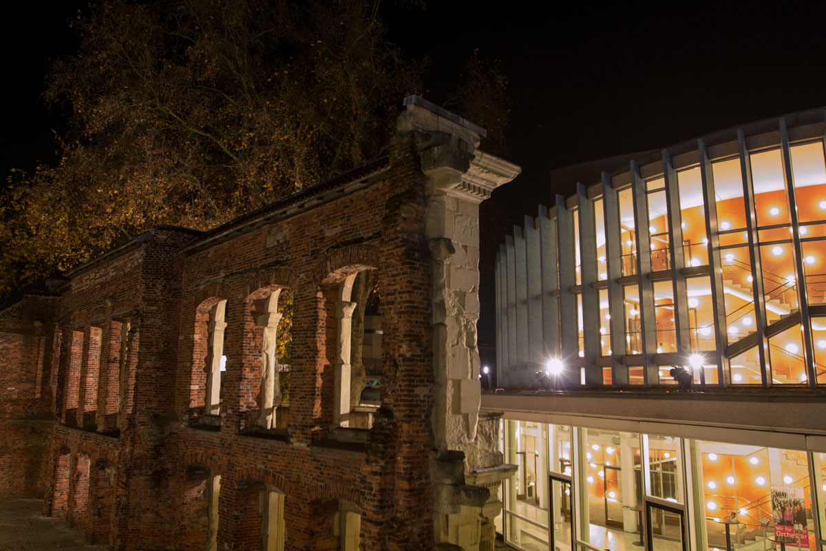 links ist eine alte Gebäudefassade zu sehen, rechts der rundförmige Glasbau des Theaters Münster